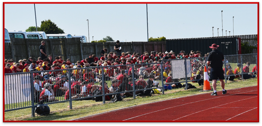students sat down listening to a teacher at sports day